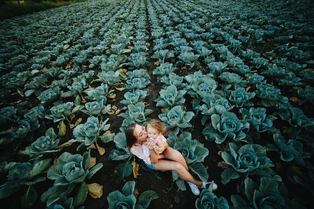 Мать с дочерью сидит на вершине ее в поле капустой
