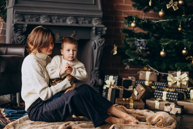 クリスマスツリーのそばに座って彼女の幼い息子を持つ母