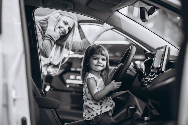 Mother with little daughet sitting in a car in a car showroom