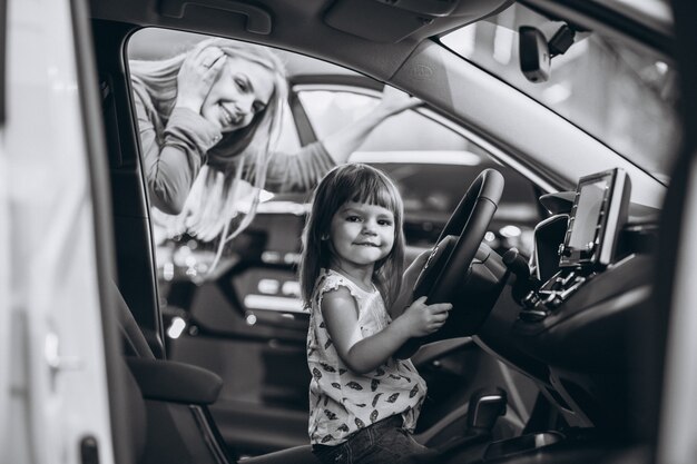 車のショールームで車に座っている小さな娘を持つ母