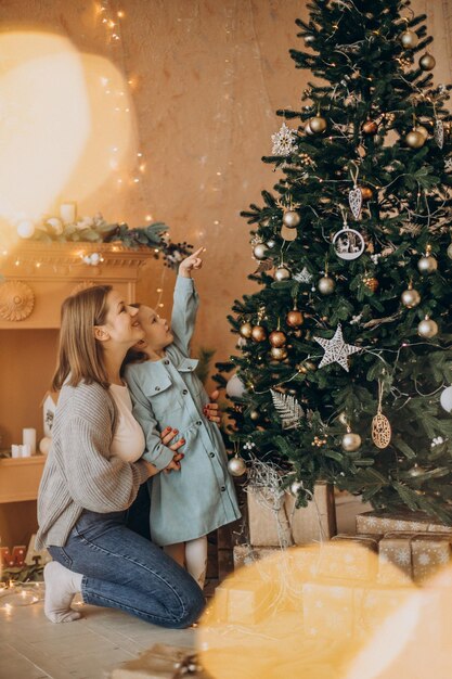장난감으로 크리스마스 트리를 장식하는 어린 딸과 함께 어머니