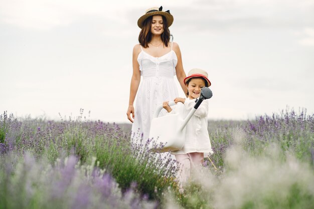 Mother with little daughter on lavender field. Beautiful woman and cute baby playing in meadow field. Family holiday in summer day.