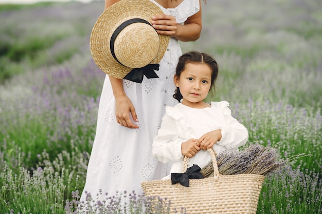 Mother with little daughter on lavender field. Beautiful woman and cute baby playing in meadow field. Family holiday in summer day.