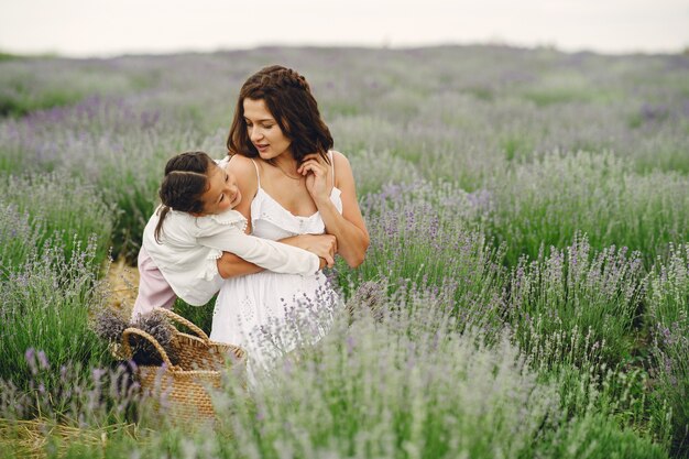 ラベンダー畑に小さな娘を持つ母。美しい女性と牧草地で遊ぶかわいい赤ちゃん。夏の日の家族の休日。