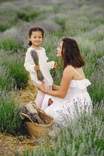 Mother with little daughter on lavender field. Beautiful woman and cute baby playing in meadow field. Family holiday in summer day.