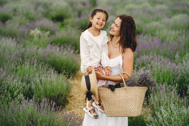 Mother with little daughter on lavender field. Beautiful woman and cute baby playing in meadow field. Family holiday in summer day.