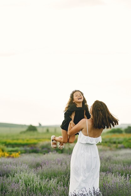 Mother with little daughter on lavender field. Beautiful woman and cute baby playing in meadow field. Family holiday in summer day.