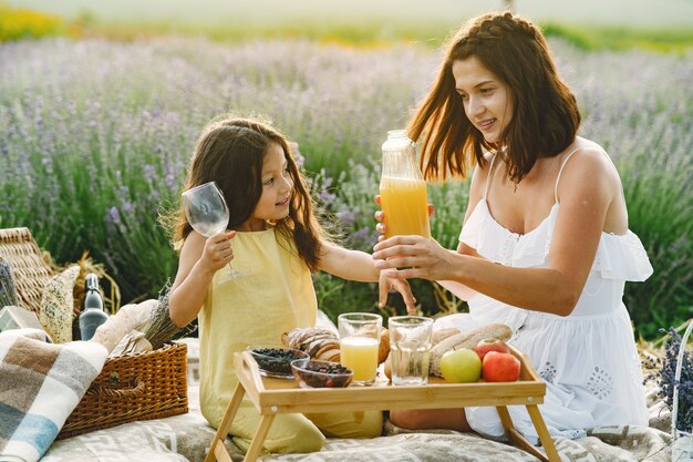 Mother with little daughter on lavender field. Beautiful woman and cute baby playing in meadow field. Family in a picnic.