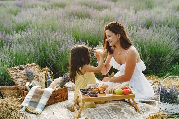 Mother with little daughter on lavender field. Beautiful woman and cute baby playing in meadow field. Family in a picnic.