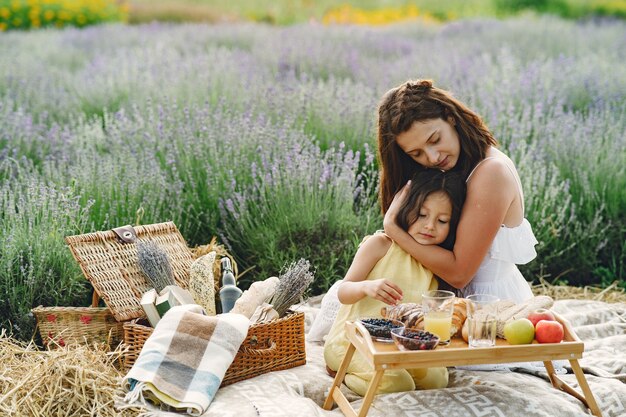 Mother with little daughter on lavender field. Beautiful woman and cute baby playing in meadow field. Family in a picnic.