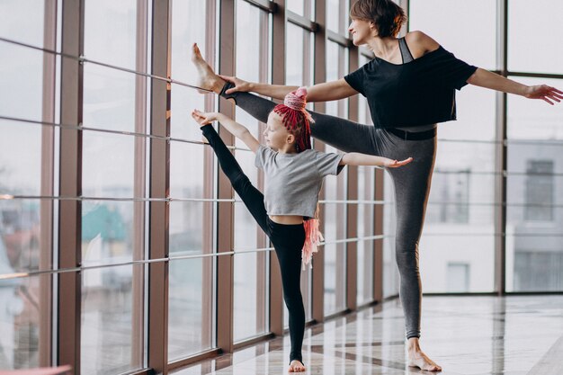 Mother with little daughter practicing yoga by the window