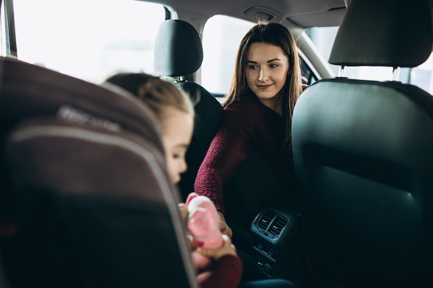 Mother with little daughter sitting in the back of the car in a car seat