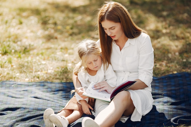 Mother with little daughter sitting on a plaid and read the book