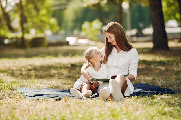 Mother with little daughter sitting on a plaid and read the book