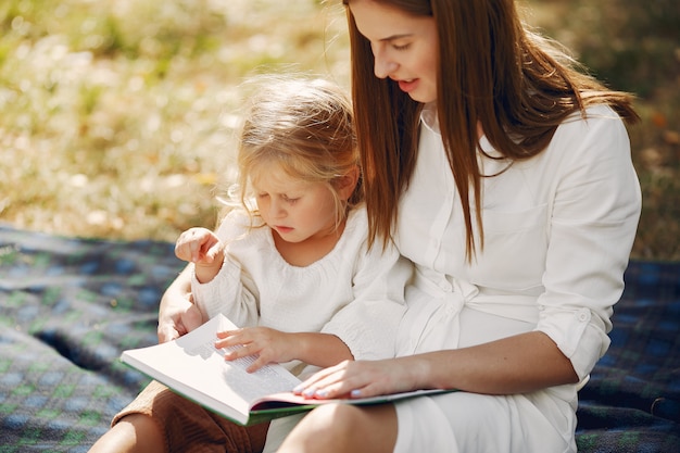 Mother with little daughter sitting on a plaid and read the book
