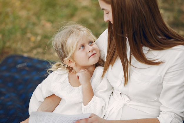 Mother with little daughter sitting on a plaid and read the book