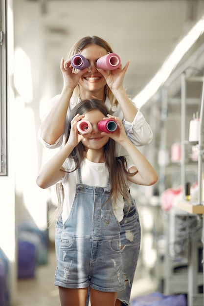 Free photo mother with little daughter standing at the fabric with thread