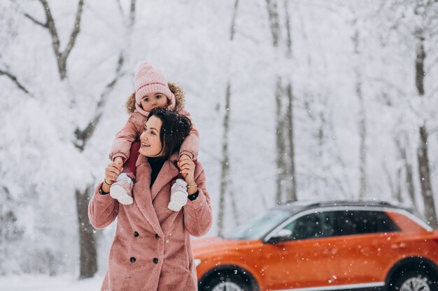 Mother with little daughter in a winter park by car