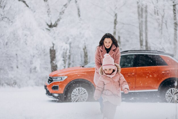 Mother with little daughter in a winter park by car