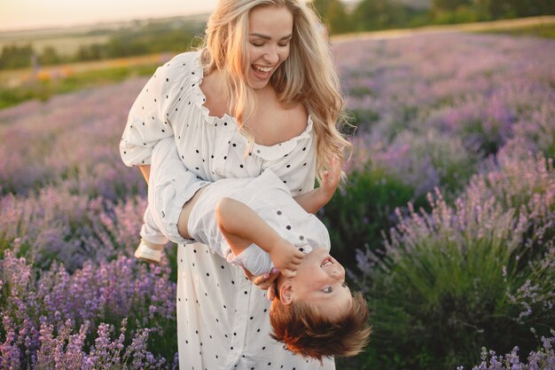 Mother with little son on lavender field. Beautiful woman and cute baby playing in meadow field. Family holiday in summer day.