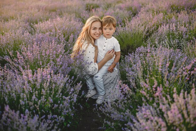 Mother with little son on lavender field. Beautiful woman and cute baby playing in meadow field. Family holiday in summer day.