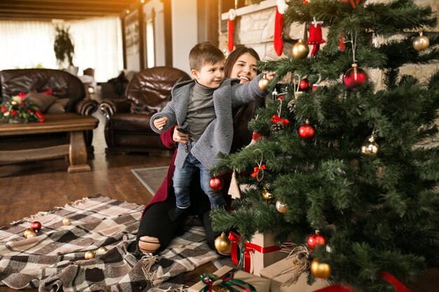 Mother with son on Christmas by the fir-tree