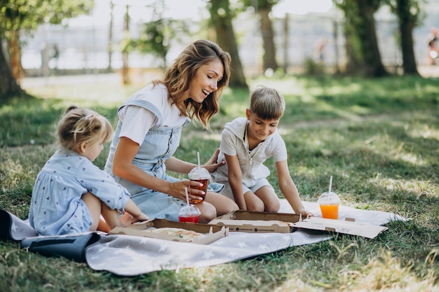Madre con figlio e figlia che mangiano pizza nel parco