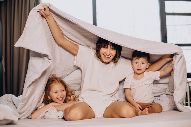 Free photo mother with son and daughter sitting on bed under the blanket