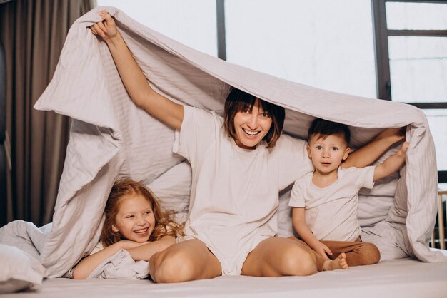 Мать с сыном и дочерью сидят на кровати под одеялом