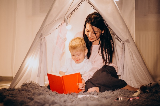 Mother with son sitting in cozy tent with lights at home on christmas