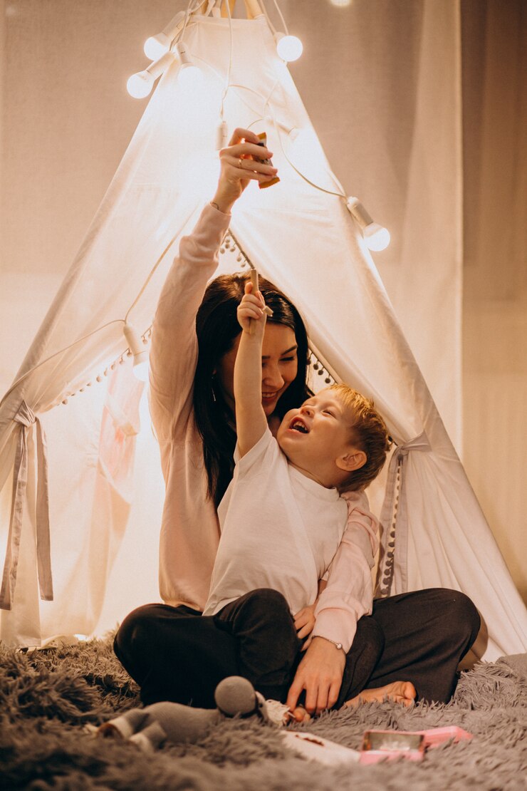 Free Photo mother with son sitting in cozy tent with lights at home on christmas