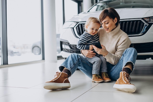 Mother with son using phone by the car in a car showroom