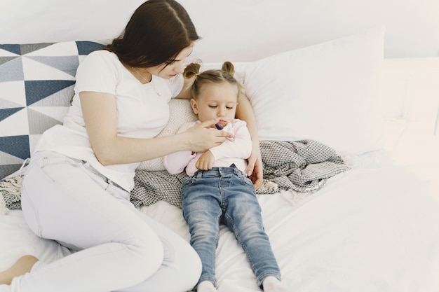 Mother with thermometer is sitting near daughter