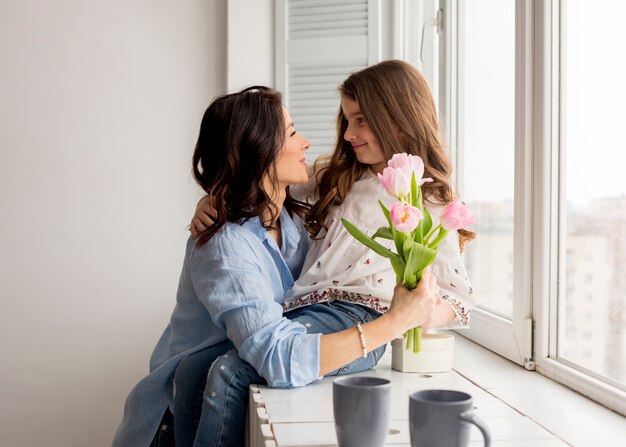 Mother with tulips hugging daughter at window 