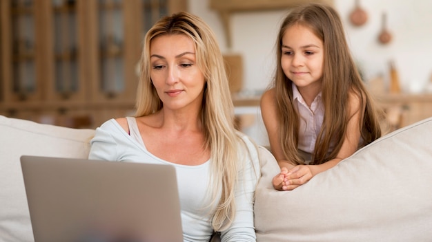 Foto gratuita madre che lavora al computer portatile da casa con la figlia a guardare