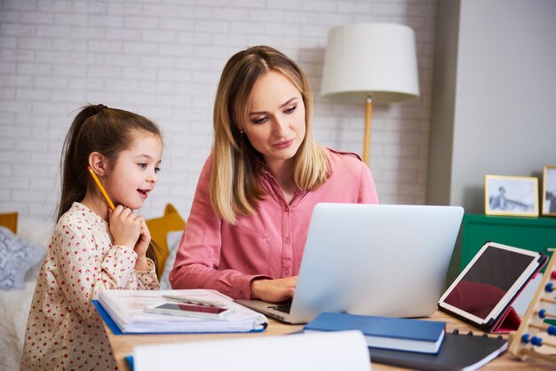 Mother working with little daughter at home interior