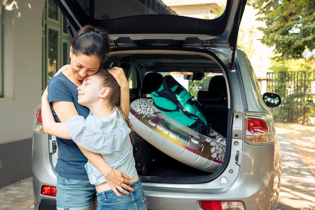 母と幼い子供が海辺での休暇旅行に出かける前に抱き合い、車のトランクに荷物やスーツケースを積み込む。荷物とインフレータブル、レジャー レクリエーションを持って夏休みに出発します。