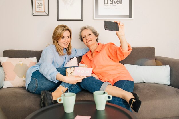 Mothers and daughter taking selfie on couch