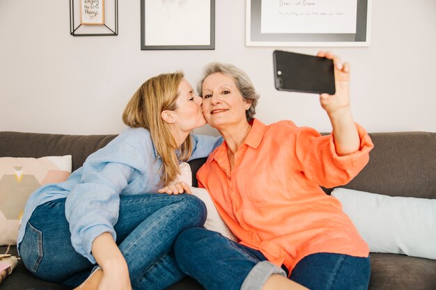 Mothers and daughter taking selfie in living room