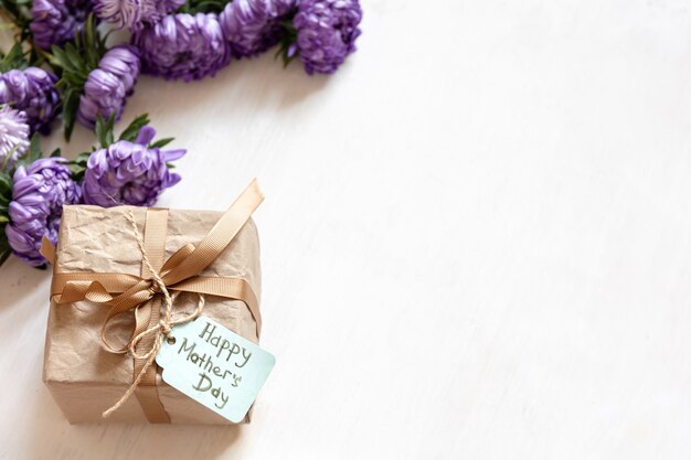 Mothers day festive background with gift box and fresh chrysanthemum flowers on white background, copy space.