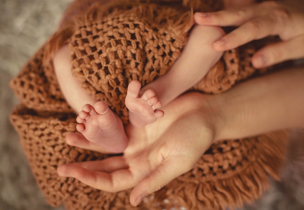 Mothers hands hold cute and little legs of newborn baby