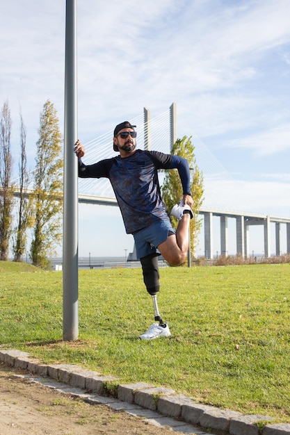 Бесплатное фото Мотивированный мужчина с искусственной ногой готовится к пробежке. мужчина в спортивной одежде растягивается в парке в летний день, тренируется. спорт, тренировки, благополучие, концепция инвалидности