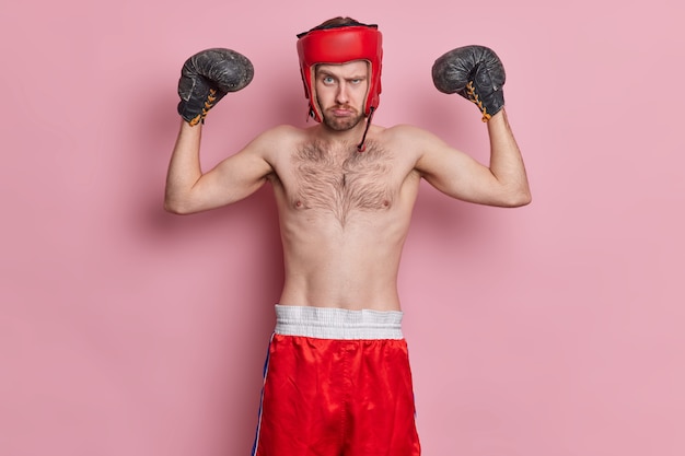 동기 부여 스포츠맨은 권투를 즐기고 보호 모자 장갑을 끼고 팔을 들어 근육을 보여줍니다.