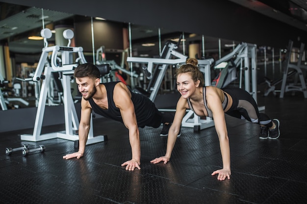 Motivated young blond woman and man in middle of workout, standing in plank with hands clenched together.