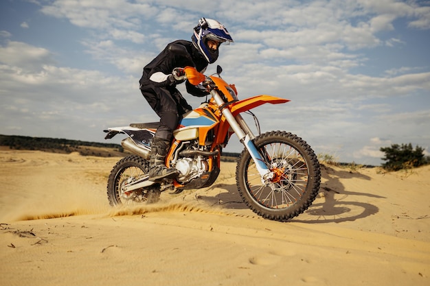 바퀴 아래에서 먼지를 날리는 오프로드 자전거를 더 아래로 모래 언덕에서 운전하는 motocross 라이더