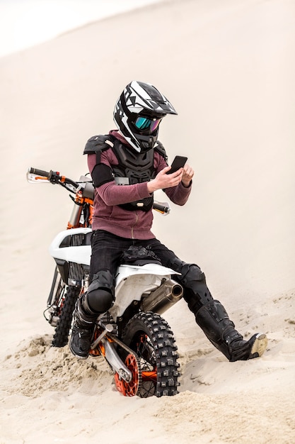 Мотоциклист с шлемом просматривает мобильный телефон