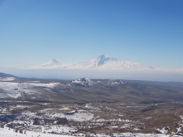 アルメニアの昼間の日光の下で雪に覆われたフィールドに囲まれたアララット山