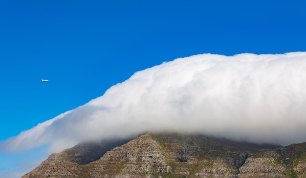 Roccia di montagna coperta dalle nuvole di un aeroplano che vola nel cielo blu