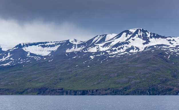 アイスランドの憂鬱な日に海の近くの雪に覆われた写真の山