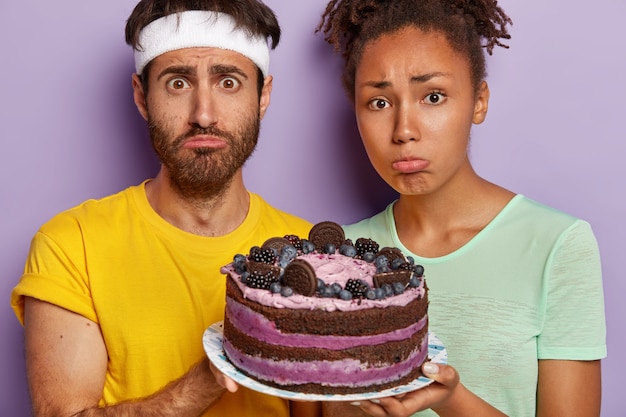 mournful active couple posing with a big cake